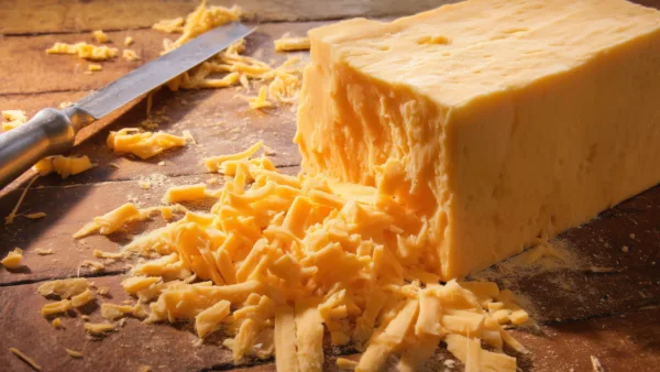 Сыр чеддер на деревянной доске с тёркой и кусочками сыра