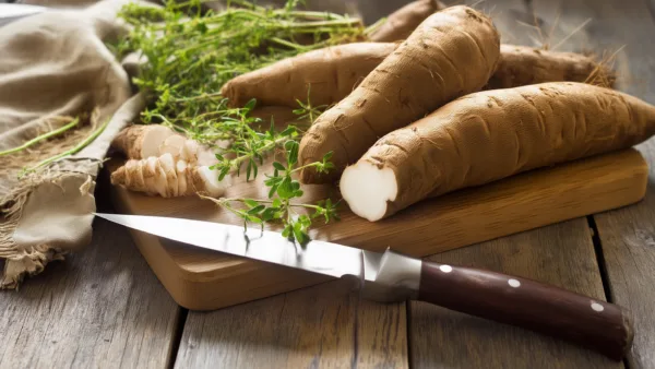 Свежие клубни ямса с ножом и зеленью на деревянной доске