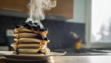 Фото блюда: Воздушные панкейки с голубикой и сиропом на сковороде